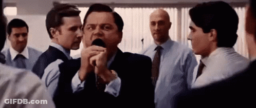 A Man In A Suit Is Talking Into A Microphone While Standing In A Crowd Of People . GIF