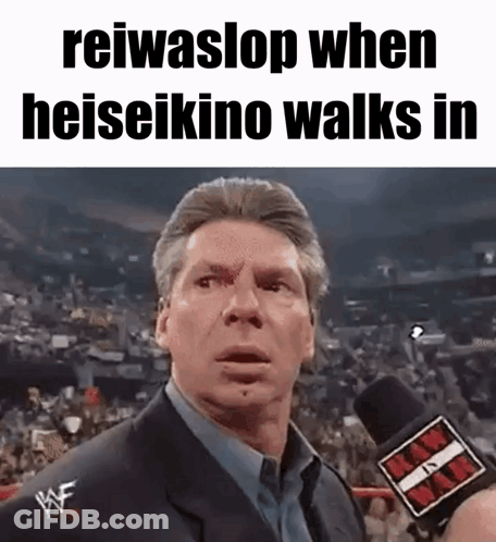 A Man In A Suit Is Talking Into A Microphone While Standing In Front Of A Crowd . GIF