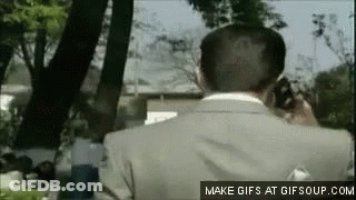 A Man In A Suit Is Talking On A Cell Phone In The Park . GIF