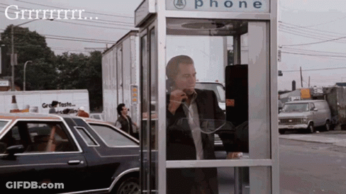 A Man In A Suit Is Talking On A Phone In A Phone Booth GIF