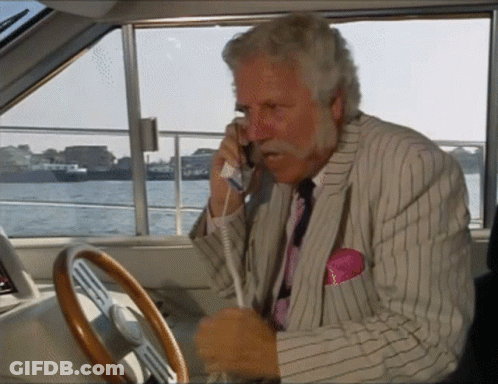 A Man In A Suit Is Talking On A Phone While Driving A Boat GIF