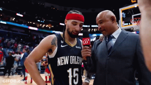 A Man In A Suit Is Talking To A Basketball Player In A New Orleans Jersey GIF