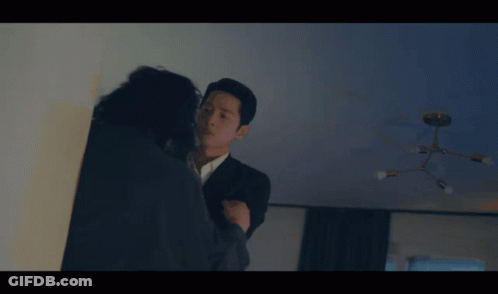 A Man In A Suit Is Talking To A Woman In A Dark Room GIF