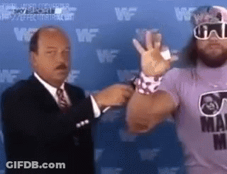 A Man In A Suit Is Talking To A Wrestler In A Purple Shirt . GIF