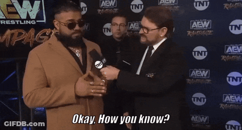A Man In A Suit Is Talking To Another Man In Front Of A Wall That Says Aew GIF