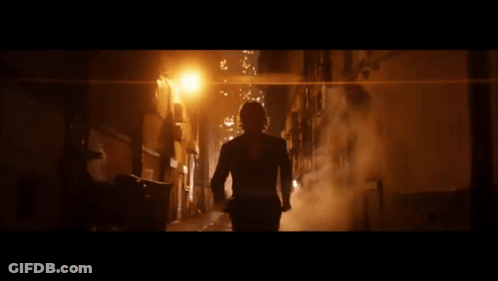 A Man In A Suit Is Walking Down A Dark Alley At Night GIF