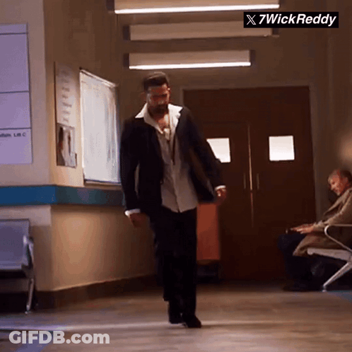 A Man In A Suit Is Walking Down A Hallway With A Sign That Says X7wick Reddy On It GIF