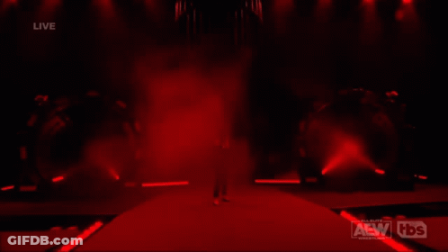 A Man In A Suit Is Walking Down A Red Carpet In Front Of A Live Aew Wrestling Event GIF