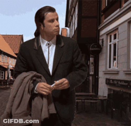 A Man In A Suit Is Walking Down A Street In Front Of A Building With A Sign That Says Kaiser 'S GIF