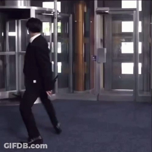 A Man In A Suit Is Walking In Front Of A Door That Says ' Exit ' On It GIF