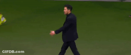 A Man In A Suit Is Walking On A Soccer Field While A Person Throws A Yellow Shoe . GIF