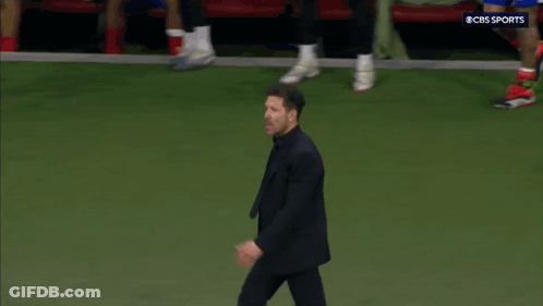 A Man In A Suit Is Walking On A Soccer Field With A Cbs Sports Logo In The Background GIF