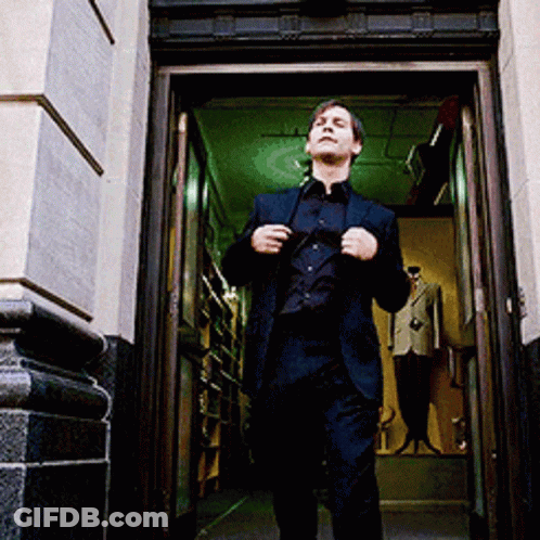 A Man In A Suit Is Walking Out Of A Doorway GIF