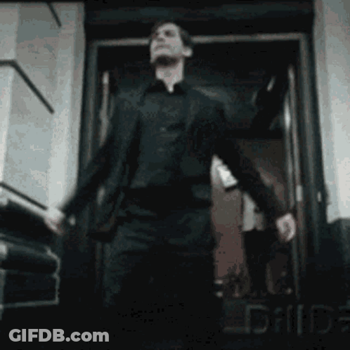 A Man In A Suit Is Walking Out Of A Doorway . GIF