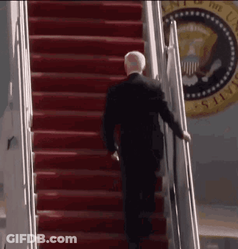 A Man In A Suit Is Walking Up The Stairs Of A Plane . GIF