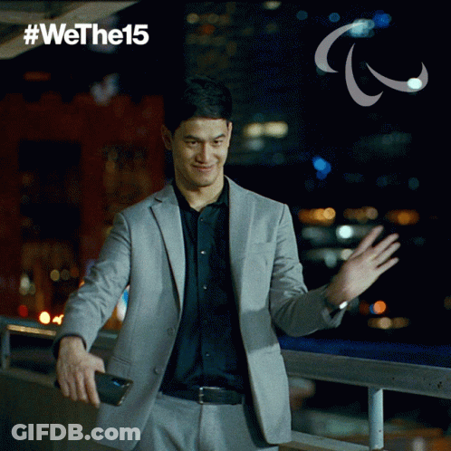 A Man In A Suit Is Waving His Hand In Front Of A Sign That Says #Wethel5 GIF