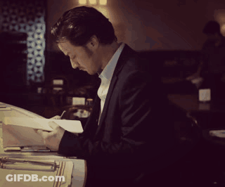 A Man In A Suit Is Writing On A Piece Of Paper In A Dark Room GIF