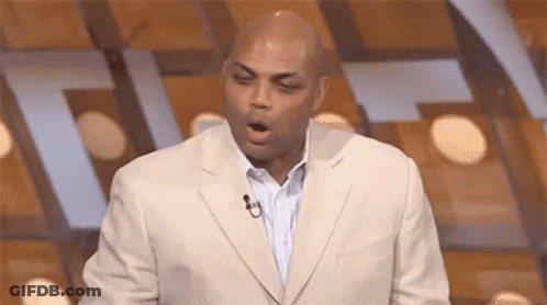 A Man In A Suit Is Yawning While Standing In Front Of A Microphone On A Stage . GIF