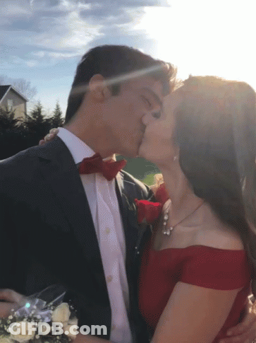A Man In A Suit Kisses A Woman In A Red Off The Shoulder Dress GIF