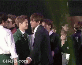 A Man In A Suit Kisses Another Man In A Crowd Of People GIF