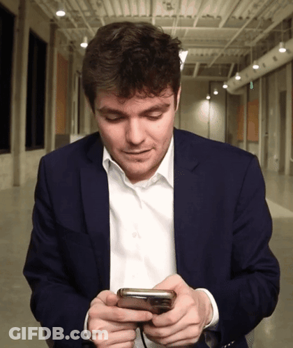 A Man In A Suit Looks At His Cell Phone GIF