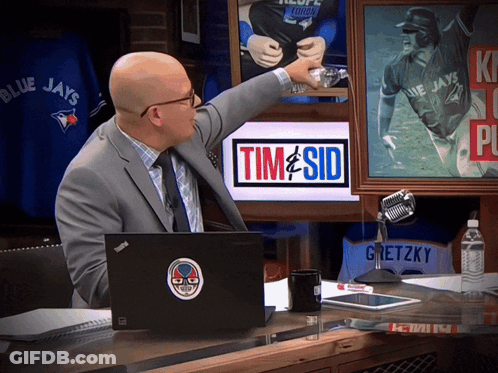 A Man In A Suit Points To A Picture Of A Blue Jays Baseball Player GIF