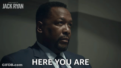 A Man In A Suit Says Here You Are In Front Of A Poster For Tom Clancy 'S Jack Ryan GIF