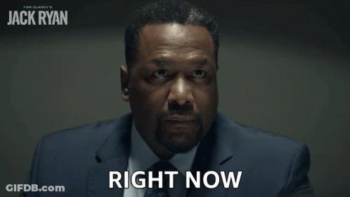A Man In A Suit Says Right Now In Front Of A Poster For Jack Ryan GIF