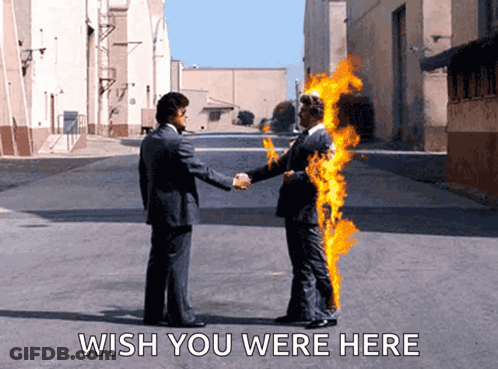 A Man In A Suit Shakes Hands With A Man In A Burning Suit With The Words Wish You Were Here Below Them GIF