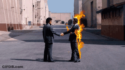 A Man In A Suit Shakes Hands With A Man In A Fire Suit GIF