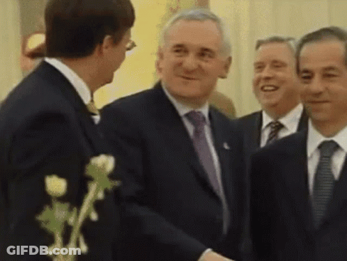 A Man In A Suit Shakes Hands With Another Man In A Suit And Tie GIF