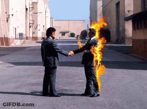 A Man In A Suit Shakes Hands With Another Man In A Suit That Is On Fire GIF