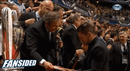 A Man In A Suit Shakes Hands With Another Man In Front Of A Crowd With The Words Fansided On The Bottom Right GIF