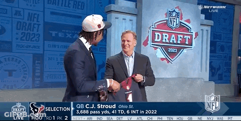 A Man In A Suit Shakes Hands With Another Man In Front Of A Nfl Draft Sign GIF