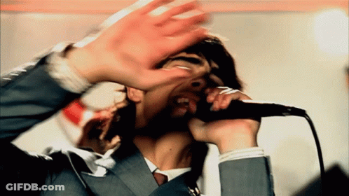 A Man In A Suit Singing Into A Microphone With His Hands Up GIF