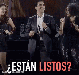 A Man In A Suit Singing Into A Microphone With The Words " Estan Listos " In Red GIF