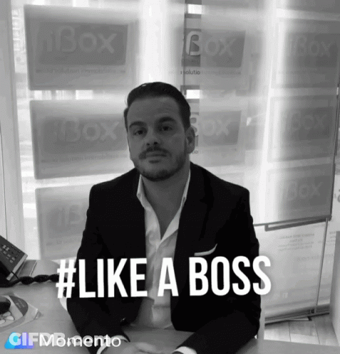 A Man In A Suit Sits At A Desk In Front Of A Window That Says Box On It GIF