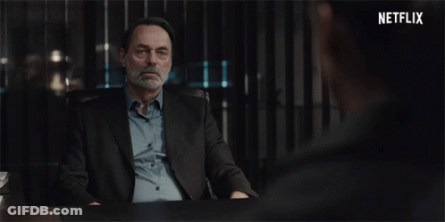A Man In A Suit Sits At A Desk With A Netflix Logo In The Corner GIF