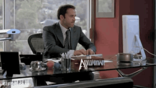 A Man In A Suit Sits At A Desk With A Sign That Says Atlantis On It GIF