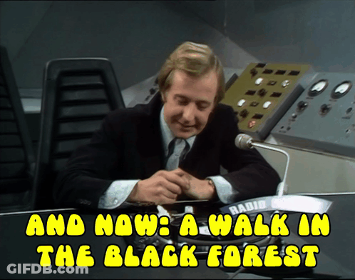 A Man In A Suit Sits At A Desk With The Words And Now A Walk In The Black Forest Above Him GIF