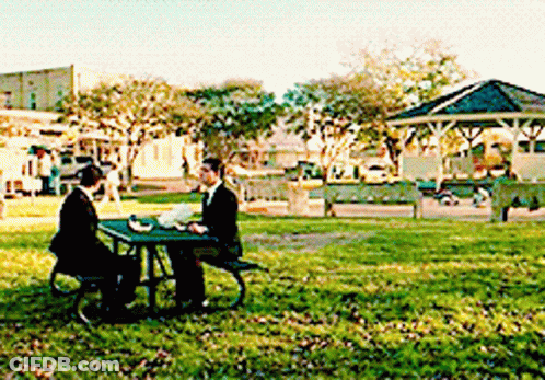 A Man In A Suit Sits At A Picnic Table In A Park GIF
