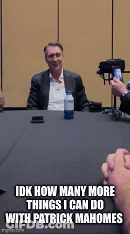 A Man In A Suit Sits At A Table With A Bottle Of Water And A Cell Phone GIF
