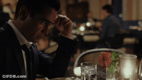 A Man In A Suit Sits At A Table With A Glass Of Water On It GIF