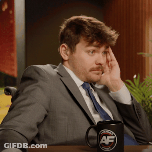 A Man In A Suit Sits At A Table With A Mug That Says America First On It GIF