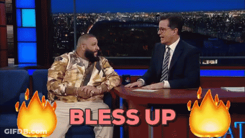 A Man In A Suit Sits At A Table With The Words Bless Up Behind Him GIF