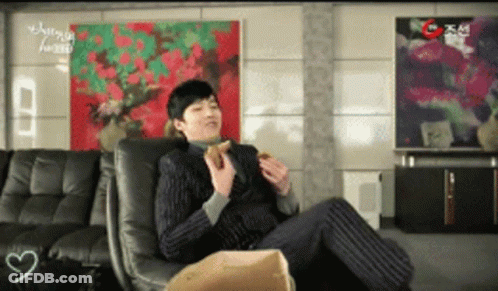 A Man In A Suit Sits In A Chair Eating A Burger GIF