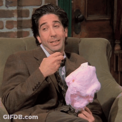 A Man In A Suit Sits In A Chair Eating Cotton Candy GIF