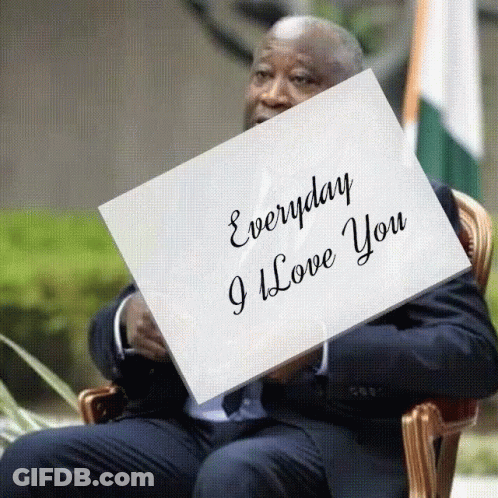 A Man In A Suit Sits In A Chair Holding A Piece Of Paper That Says Everyday I Love You GIF