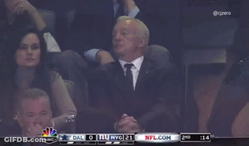 A Man In A Suit Sits In A Stadium Watching A Game Between Dallas And New York Giants GIF