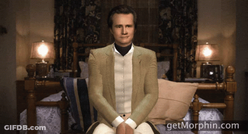 A Man In A Suit Sits In Front Of A Bed With The Website Getmorphin.com GIF